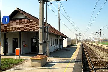 Foto zeigt Bahnhofsgebäude auf linker Seite vom Standpunkt Bahnübergang Bahnstraße mit Blickrichtung Westen, rechts der doppelte Schienenstrang